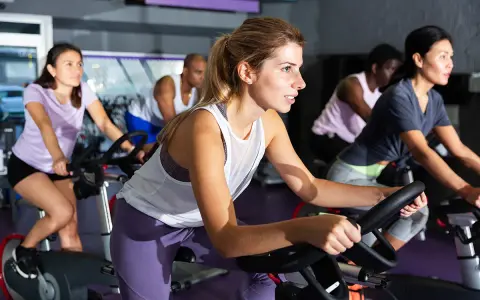 Women in a gym class experience the hiit cycling benefits, pedaling intensely on stationary bikes.