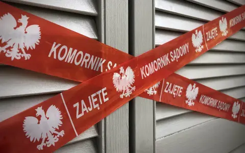 Czerwona taśma z napisem "KOMORNIK SĄDOWY" i godłem Polski krzyżuje się na szarym tle. Nakaz zapłaty w postępowaniu upominawczym a komornik.