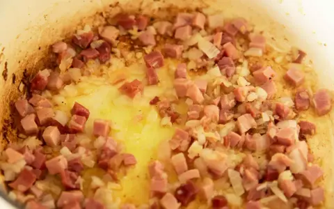 Guisantes con jamón y cebolla dorándose en una sartén con aceite. Un plato tradicional español.