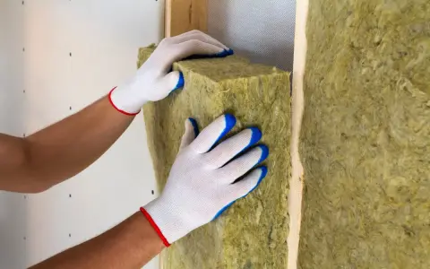 Pose d'isolant en laine de roche dans un mur. Les mains gantées ajustent le matériau pour une isolation optimale.