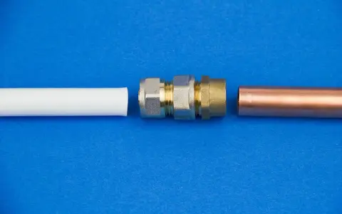 Raccordement de tuyaux : un coude 1/4 mâle femelle en laiton et un tube de cuivre à côté d'un tube blanc.