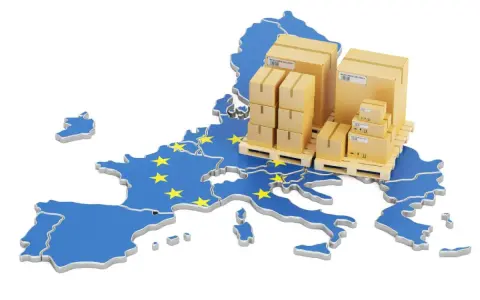 Cajas apiladas sobre palets, sobre un mapa de la Unión Europea con estrellas amarillas. Representa la logística y el comercio, y te preguntas: ¿qué es el VAT en este contexto?