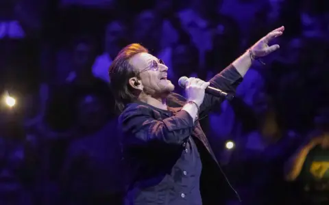 Bono z U2 śpiewa na koncercie, zapowiadając u2 nowa płyta. Tłum w ciemnościach reaguje na jego występ.