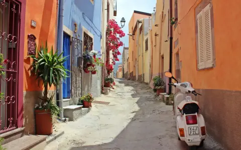 Un vicolo colorato con case arancioni e blu, fiori rossi e una Vespa bianca. Perfetto per le tue idee weekend nord Italia.