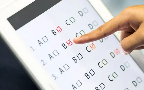 Palec wskazuje odpowiedź B na ekranie tabletu, gdzie trwa test baltimorski. Zaznaczone są już odpowiedzi B i C.