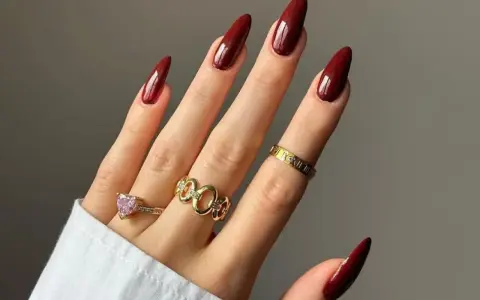Main d'une femme aux ongles longs et pointus, vernis d'un profond couleur vernis automne. Bagues dorées ornées de pierres et de motifs.