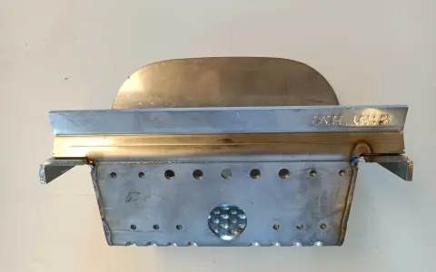 Un abbattitore di fumi per stufe a pellet, realizzato in metallo, con fori e un'area traforata.