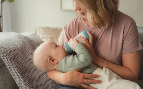 Mutter füttert Baby mit Flasche. Das Baby trinkt langsam, um die Verdauung zu unterstützen.