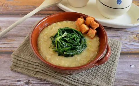 Piatto di fave e cicoria, una crema gialla con verdura verde al centro e crostini dorati.