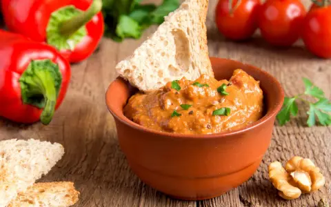Un saporito pesto di peperoni in una ciotola di terracotta, accompagnato da crostini, noci e peperoni rossi freschi.