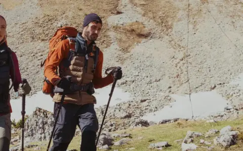 Para idąca szlakiem Gerlach. Kobieta i mężczyzna w górskim terenie, z plecakami i kijkami trekkingowymi, przemierzają kamienisty teren.
