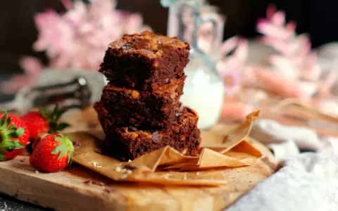 Saftige brownies rezept: Ein Stapel Schokoladenkuchen mit Nüssen, garniert mit frischen Erdbeeren und einem Krug Milch.