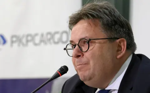 Mężczyzna w okularach przed mikrofonem na tle logo PKP Cargo.