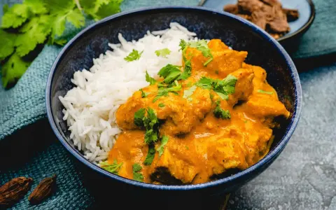 Cremiges Chicken Korma mit Basmatireis, garniert mit frischem Koriander. Ein köstliches indisches Gericht.