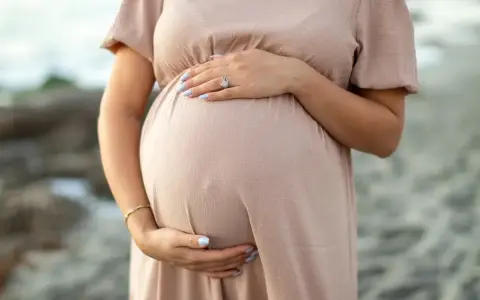 Brzuch kobiety w ciąży, delikatnie otulony dłonią. W trosce o zdrowie maluszka, przyszła mama unika kosmetyków z retinolem.