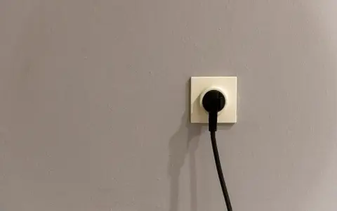 Gniazdko elektryczne z wtyczką na szarej ścianie. Czy to symbol energa taryfa urzędowa?