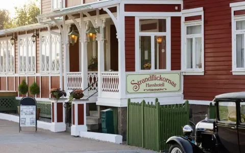 Strandflickornas Havshotell i Lysekil, en charmig röd byggnad med vita detaljer, välkomnar besökare. En klassisk bil står parkerad framför.