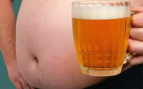 Ein Bierbauch, der zeigt, dass Bier dick macht. Eine Hand hält ein Glas Bier vor dem Bauch.