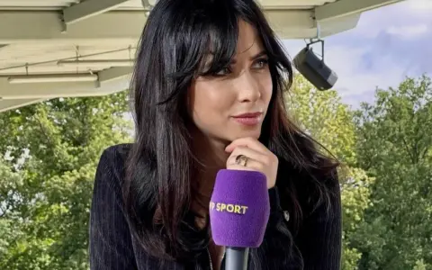 Maja Strzelczyk, dziennikarka sportowa, z mikrofonem Polsat Sport. W tle zielone drzewa i niebo.