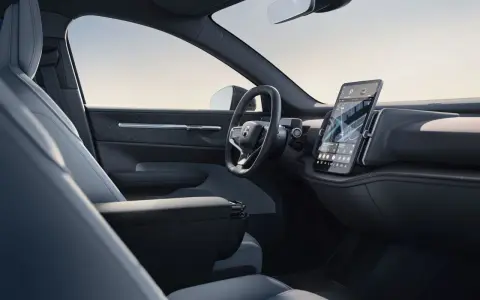 Interni minimalisti del Volvo EX30: sedili chiari, volante moderno e grande schermo centrale con navigazione.