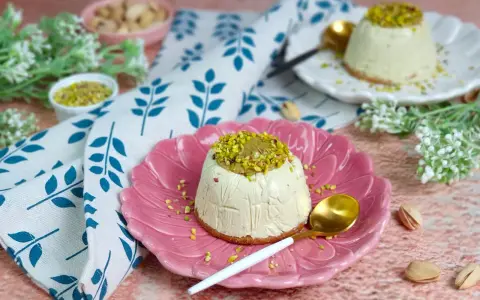 Delizioso semifreddo al pistacchio, guarnito con crema e granella di pistacchi, servito su un piatto rosa.
