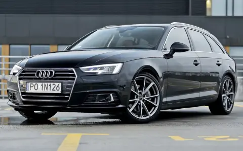 Czarny Audi A4 Avant, model b9, zaparkowany na mokrym parkingu z żółtymi liniami.