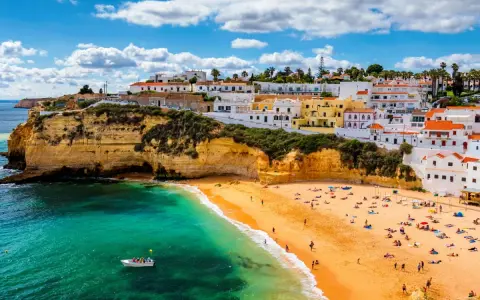 Coastal town with white buildings on cliffs overlooking a sandy beach and turquoise water.