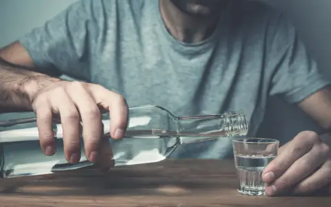 Mężczyzna nalewa alkohol do kieliszka. Nadmierne spożycie alkoholu negatywnie wpływa na żyły, prowadząc do ich uszkodzenia.
