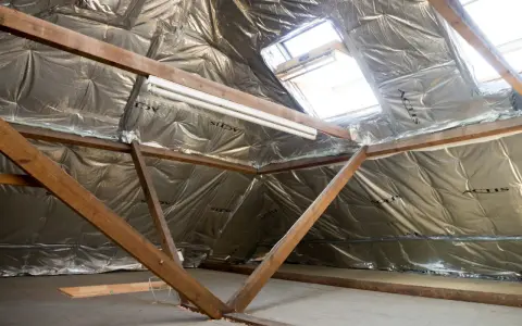 Isolation des combles 100m2 : vue d'un grenier en cours d'isolation avec matériaux réfléchissants et charpente bois.