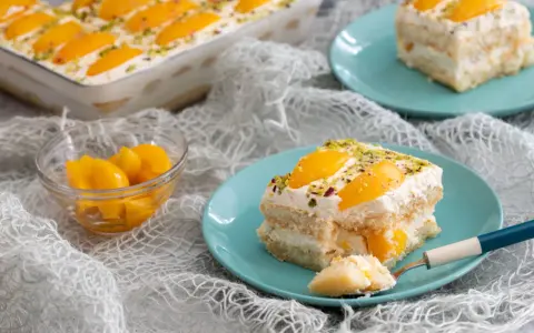 Delizioso tiramisù alle pesche, con strati di savoiardi, crema soffice e pesche sciroppate, guarnito con pistacchi.