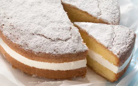 Torta paradiso sofficissima, con crema bianca e zucchero a velo. Una fetta è stata tagliata, invitando a gustarla.