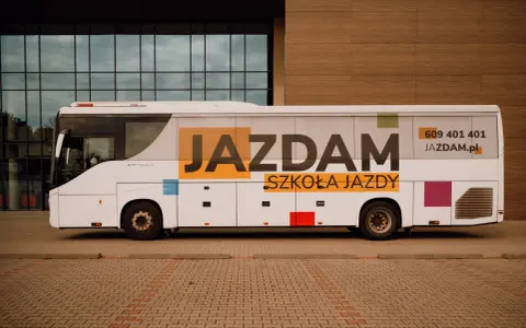 Biały autobus szkolny z napisem "JAZDAM SZKOŁA JAZDY" i numerem telefonu.