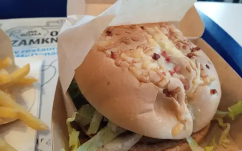 Pyszny burger drwala z chrupiącym bekonem i serem, w papierowym opakowaniu, obok porcji frytek.