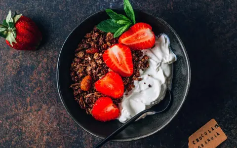 Schüssel mit Schokoladengranola, frischen Erdbeeren und cremigem Skyr oder Magerquark, garniert mit Minze.