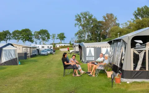 Familj njuter av en solig dag på en av Sveriges billiga campingar. Husvagnar och tält står uppradade på en grön gräsmatta.
