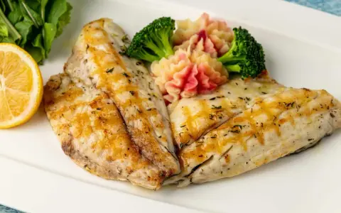 Delicioso gallo a la plancha con puré de patatas rosado, brócoli y rodaja de limón.