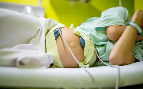 Kobieta w ciąży leży na łóżku, podłączona do aparatury KTG. Czekając na rozwój wydarzeń.