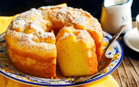 Gâteau sans gluten, saupoudré de sucre glace, sur une assiette décorée. Une part est coupée, prête à être dégustée.