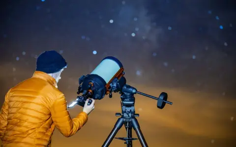 Mężczyzna w pomarańczowej kurtce ustawia aparat Canon EOS Ra do astrofotografii pod rozgwieżdżonym niebem.