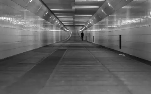 Człowiek w garniturze idzie przez długi, pusty tunel. Światła na ścianach tworzą wrażenie nieskończoności, jakby wchodził w szarą strefę.