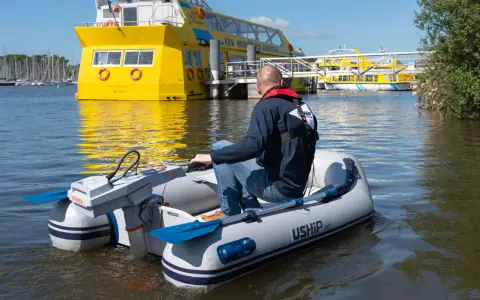 Un homme pilote un bateau gonflable propulsé par la puissance d'un moteur électrique, naviguant près d'un grand bateau jaune.