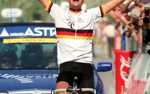 Jubelnder Radfahrer im Trikot des Teams Deutsche Telekom, ein deutscher Tour de France Sieger, mit erhobenen Armen vor jubelnder Menge.