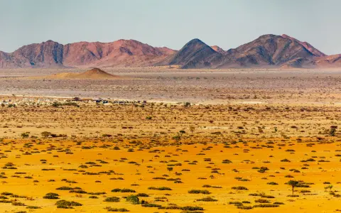 Krajobraz Namibii: pustynne równiny, góry i mała osada.