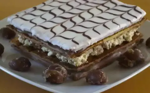 Un délicieux fondant millefeuille, garni de crème pâtissière et décoré de glaçage blanc et chocolat, est présenté sur une assiette avec quelques marrons glacés.