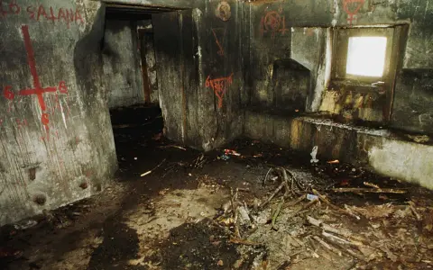 Wnętrze bunkra 44, ściany pokryte graffiti, na podłodze gruz i gałęzie.