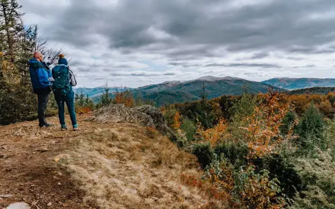 Dwóch turystów na szczycie, kamień i widok na góry. Czas przejścia przez jesienne Bieszczady.