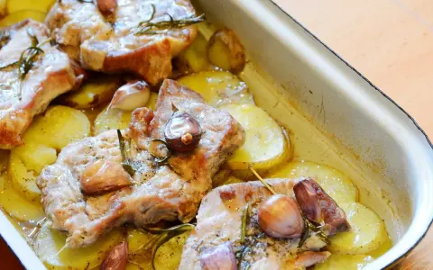 Pieczona karkówka z ziemniakami, czosnkiem i rozmarynem w naczyniu żaroodpornym.