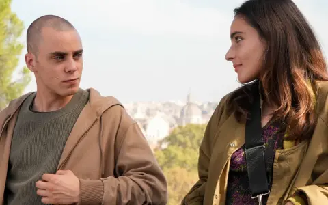 Due giovani si guardano intensamente, come se fossero in una "casa degli sguardi". Lui, rasato, lei con lunghi capelli castani.