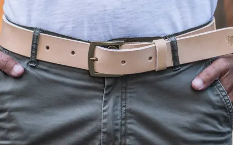 Cintura in cuoio chiaro con fibbia in ottone, indossata su pantaloni verdi. Si vede da che lato si mette la cintura.