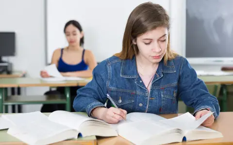 Dziewczyna w dżinsowej kurtce pisze notatki, przygotowując się do egzaminu poprawkowego.